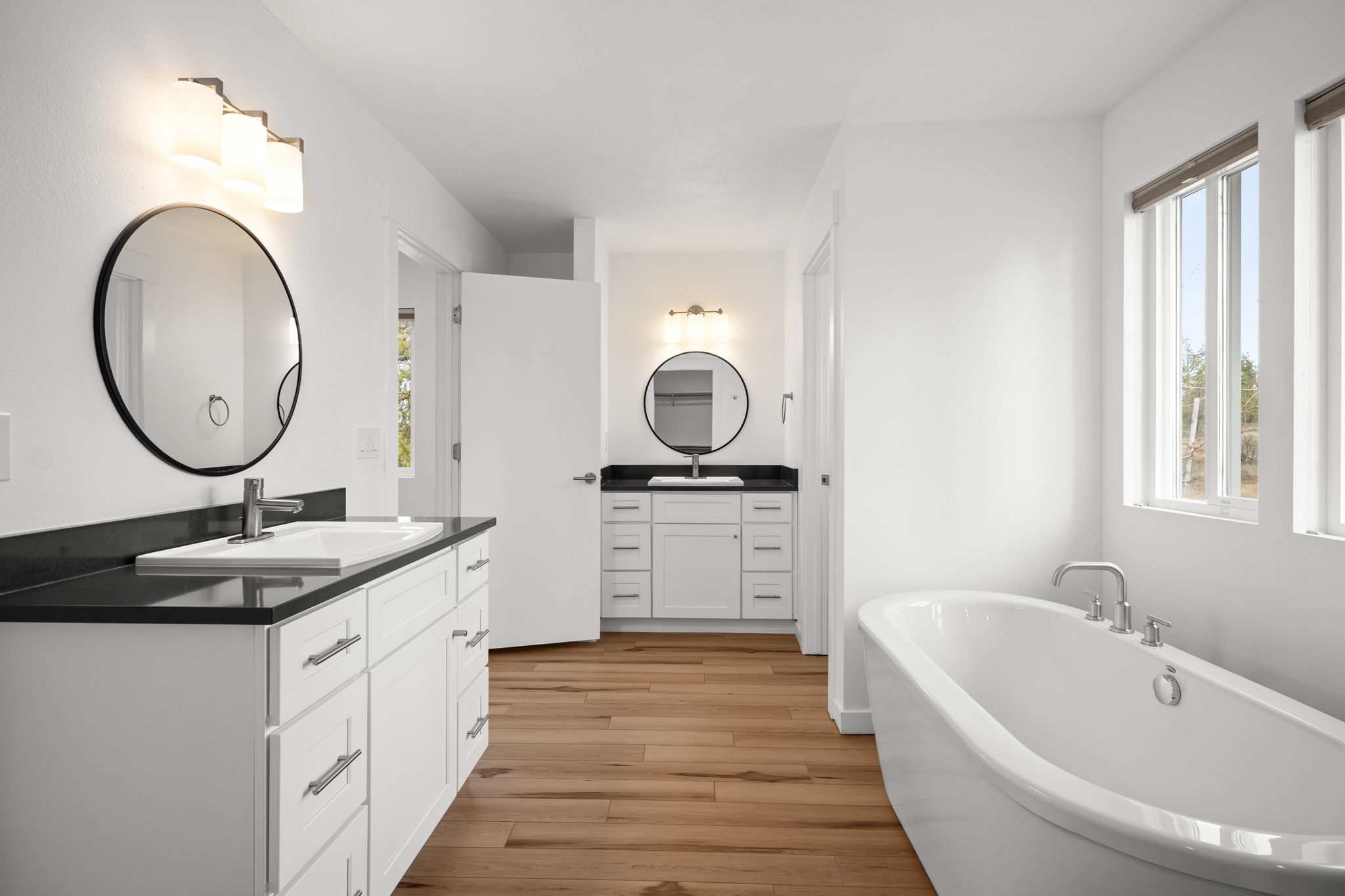 High-end bathroom with a soaking tub, double vanity, luxury vinyl plank flooring, LED lighting, and black quartz countertops