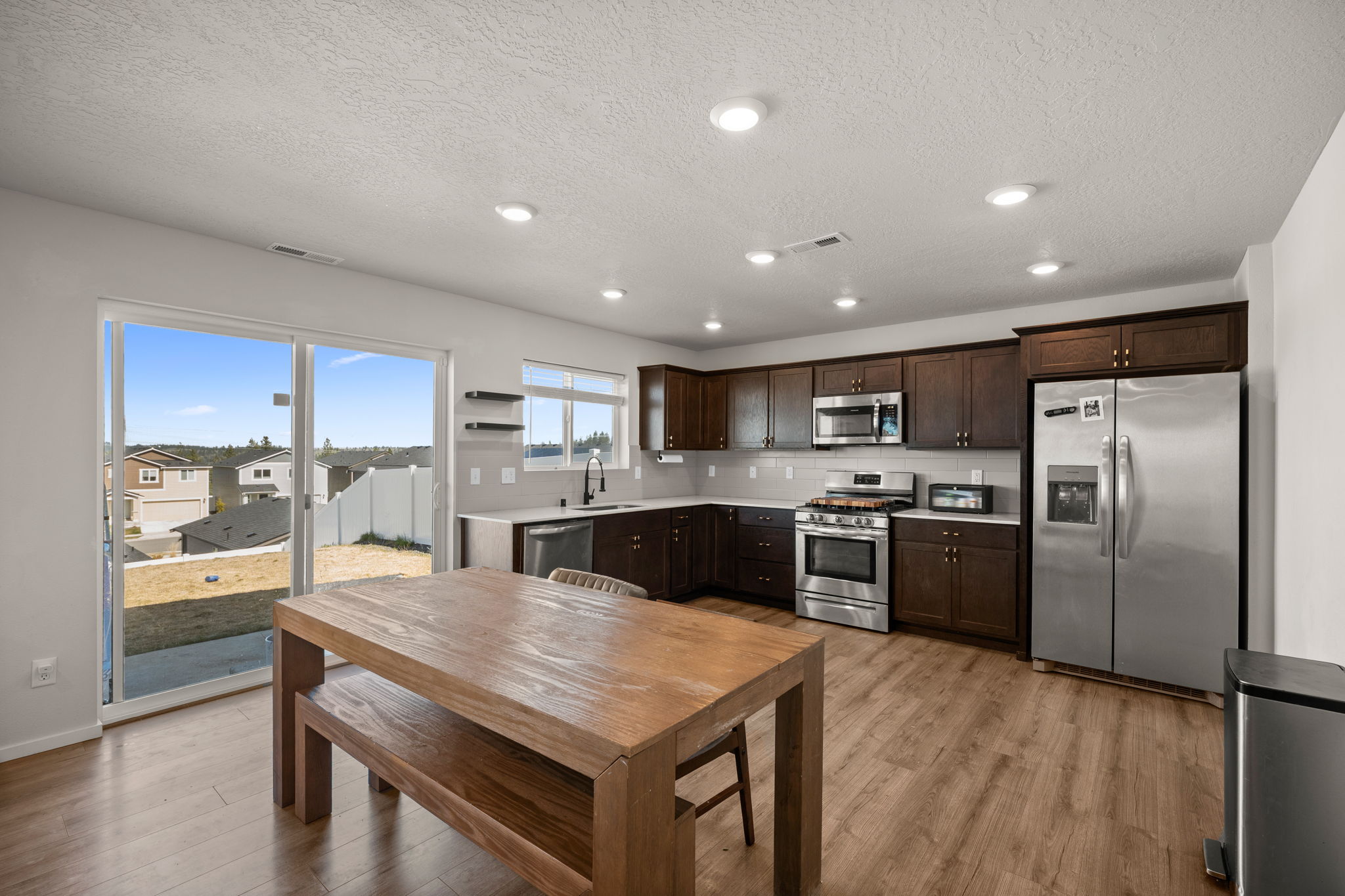 Kitchen in a new-build North Spokane home with quartz countertops, stainless steel appliances, and beautiful cabinets — green back yard visible through the back door